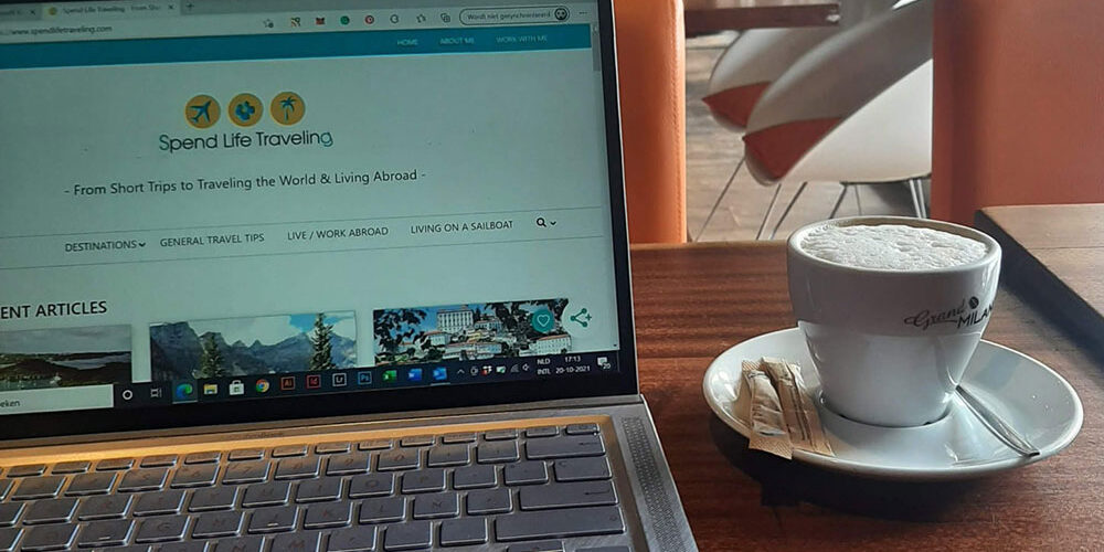 A laptop with a travel blog on the screen and a cup of coffee next to it