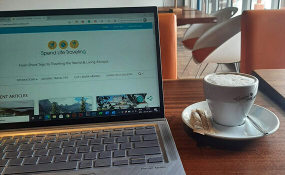 A laptop with a travel blog on the screen and a cup of coffee next to it